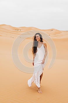 Pretty portrait of happy smiling young woman in sand dunes of Sahara desert