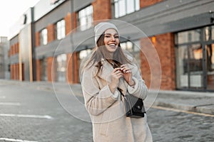 Pretty positive girl with cute smile outdoors. Fashion model of a young woman in fashionable coat in a knitted stylish hat with a