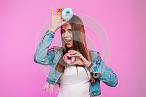 Pretty positive young woman in trendy blue jeans jacket in white t-shirt with dessert in sweet glaze posing in vintage pink wall.