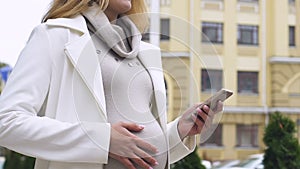 Pretty pregnant female using mobile app to navigate in big city, taxi service