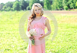 Pretty pregnant woman with chamomiles flowers in summer day