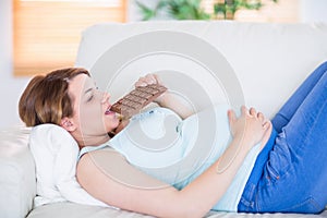 Pretty pregnant woman eating big bar of chocolate