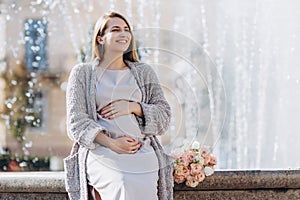 Pretty pregnant woman with flowers near the fountain. walking on the autumn street