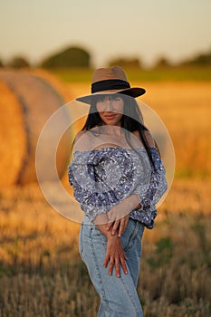 Pretty pregnant woman sexily posing for camera in nature, pregnant beauty with long black hair in straw hat