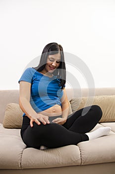 pretty pregnant woman sitting on her sofa and looking at stomach, talking to baby