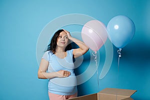 Pretty pregnant woman surprised by a gender reveal party, in anticipation of twins, expressing surprise on blue backdrop