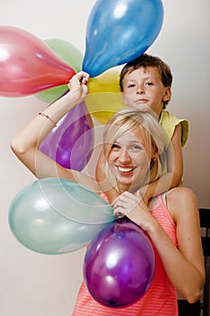 Pretty real family with color balloons on white background, blond woman with little boy at birthday party bright smiling