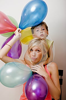 Pretty real family with color balloons on white background, blond woman with little boy at birthday party bright smiling