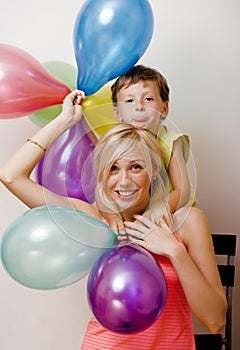 Pretty real family with color balloons on white background, blond woman with little boy at birthday party bright smiling
