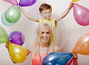 Pretty real family with color balloons on white background, blond woman with little boy at birthday party bright smiling