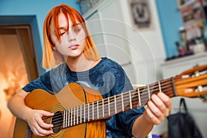 Pretty red-haired teenage girl plays guitar in her room