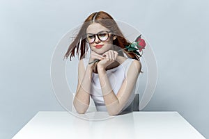 pretty red-haired woman sitting at the table with rose flower in her hands glamor red lips model