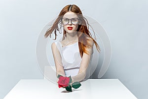 pretty red-haired woman sitting at the table with rose flower in her hands glamor red lips model