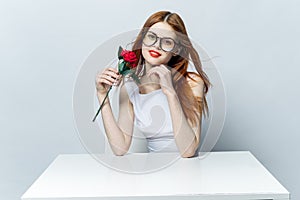 pretty red-haired woman sitting at the table with rose flower in her hands glamor red lips model