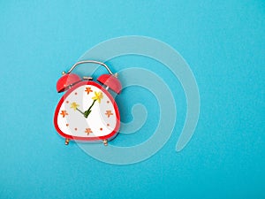 red vintage retro style alarm clock with copy space on blue background. flowers instead of dial arrows