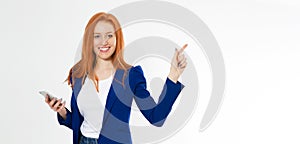 Pretty redhead girl with phone smiling pointing finger right on white background. Young foxy female in business outfit, has amazed