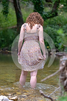Pretty redhead woman in dress walking on the river barefoot. Young woman walking barefoot, splashing water in mountain river