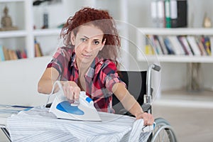 Pretty redhead woman sitting on wheelchair and ironing