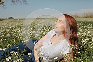 Pretty redhead woman sunbathes in the summer sun lying on a beautiful flower meadow