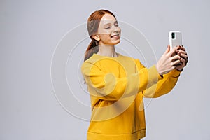 Pretty redhead young woman having video-call with lover holding smart phone in hand shooting selfie