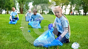 Pretty schoolgirl helping group of volunteers collecting garbage in bags at park