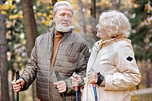 Pretty senior couple standing with nordic walking poles in colorful autumn park.