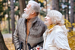 Pretty senior couple standing with nordic walking poles in colorful autumn park.