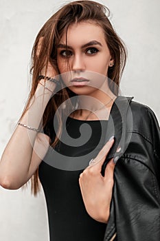 Pretty sensual young woman straightens hair. Cute attractive girl with beautiful eyes with sexy lips in a fashionable leather