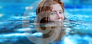 Pretty sexy, seductive, sensual redhead woman portrait relaxes swimming in turquoise, blue thermal bath hot water pool, happy