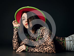 Pretty sexy smiling brunette woman in leopard patterned longsleeve, jeans and hat lying on floor looking at camera
