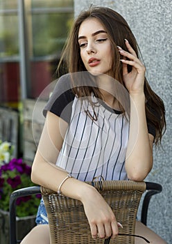 Pretty sexy young hipster woman in a T-shirt i on a straw chair outdoors in a cafe on a summer day. Attractive brunette