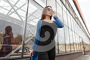 Pretty sexy young woman hipster in stylish black top in a knitted cape in trendy jeans in dark sunglasses is posing