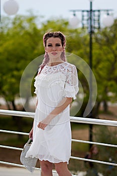 Pretty sexy young woman in a white dress posing in a park