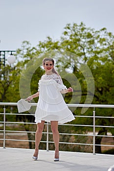 Pretty sexy young woman in a white dress posing in a park