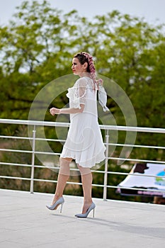 Pretty sexy young woman in a white dress posing in a park