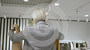 Pretty short haired woman is choosing clothes at clothing store dressed in a grey suit, tracking shot, 360 degree, close