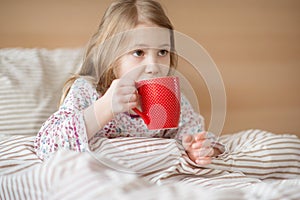 Pretty sick little child girl laying in bed drink tea