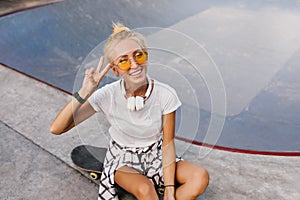 Pretty skater girl with trendy hairstyle posing with peace sign. Fashionable tanned lady in headphon