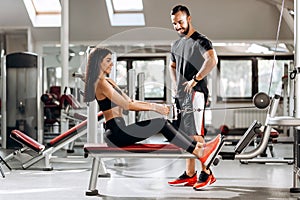 Pretty slim girl is doing exercises for the abdominals on a special exercise machine under the supervision of a coach in