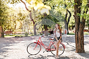 Pretty slim girl sitting on red bike. Jocund stylish woman enjoying active weekend.