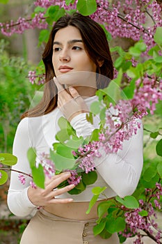 Pretty, slim girl wearing stylish clothes, looking forward, holding lilac by hands.