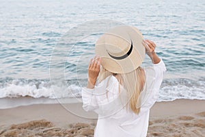 Pretty slim tanned blonde stylish woman in a straw hat posing on a paradise