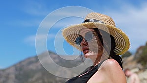 Pretty slim woman in bikini and straw floppy hat walking lies