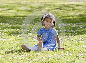 A pretty smile young girl is sitting on green meadow in spring day