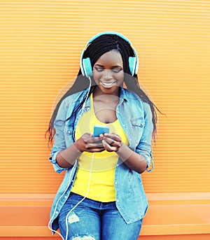 Pretty smiling african woman with headphones listens to music over orange