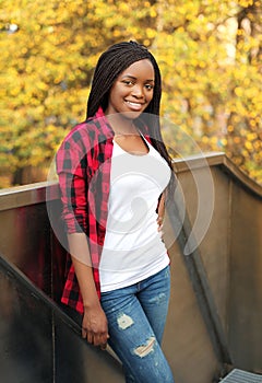 Pretty smiling african woman wearing red checkered shirt in city