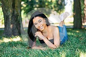 Pretty smiling afro american woman relaxing in park lying on green grass