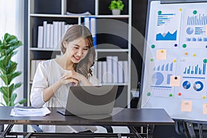Pretty smiling asian female accountant working on laptop computer in modern office