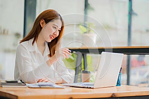 Pretty smiling asian female accountant working on laptop computer in modern office