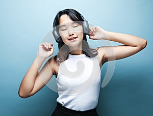 Pretty smiling Asian teenage girl listens to music on headphones over blue background.